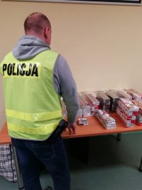 funkcjonariusz w policyjnej kamizelce układa wyroby tytoniowe