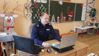 umundurowany policjant prowadzi prelekcję on-line z uczniami przed komputerem