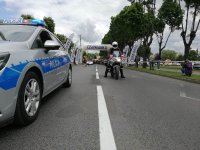 umundurowany policjant na motocyklu i oznakowany radiowóz zabezpieczają przejazd wyścigu kolarskiego