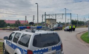 policyjny radiowóz w tle przejazd kolejowy i policjanci wraz z przedstawicielami kolei rozdają ulotki kierującym