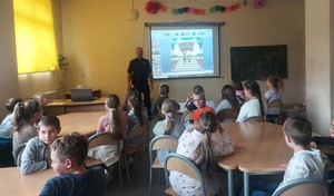 umundurowany policjant prowadzi prelekcję dla dzieci ze Szkoły Podstawowej nr 3 w Brzezinach