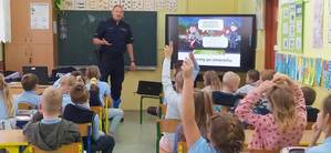 umundurowany policjant prowadzi prelekcję dla uczniów Szkoły Podstawowej nr 1 w Brzezinach