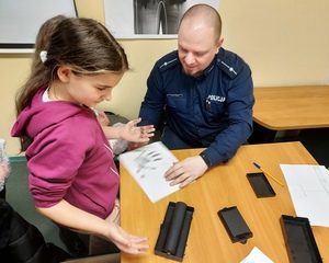 dziewczynka z policjantem w mundurze prowadzą praktyczny pokaz daktyloskopii.