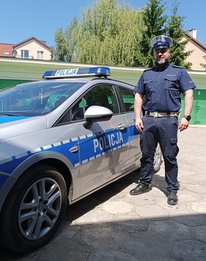 umundurowany policjant aspirant Łukasz Miazek stoi przy oznakowanym policyjnym radiowozie.
