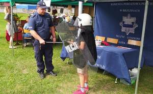 umundurowany policjant na stoisku policyjnym prezentuje dzieciom resortowy sprzęt.