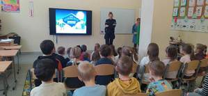 dzieci słuchają prelekcji o bezpiecznych feriach wygłaszanej przez umundurowaną policjantkę.