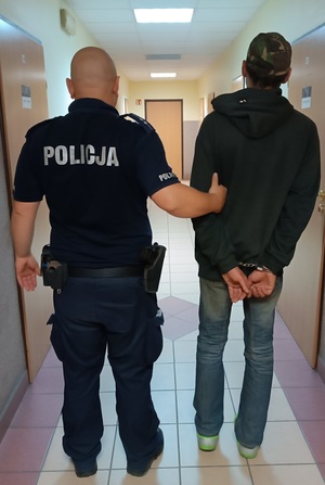 umundurowany policjant prowadzi zatrzymanego mężczyznę.