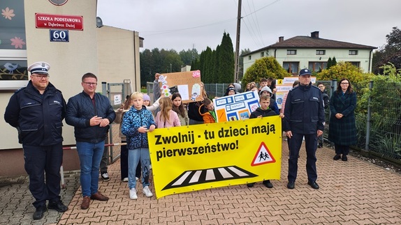 wszyscy uczestniczący w montowaniu banneru stoją na tle szkoły.