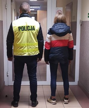 nieumundurowany funkcjonariusz w kamizelce z napisem Policja prowadzi jedną z zatrzymanych sióstr.