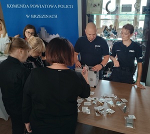 osoby oglądają policyjne stoisko z walizką edukacyjną, a umundurowani policjanci tłumaczą co się w niej znajduje.