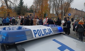 Napis Policja, a w tle uczestnicy uroczystości.