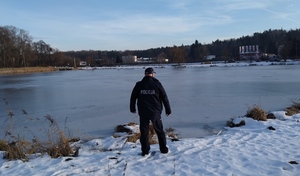 umundurowany policjant stoi nad zamarzniętym stawem.