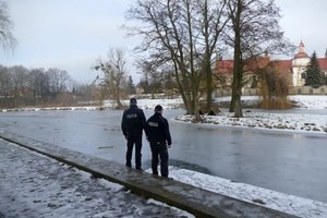 dwaj umundurowani policjanci stoją nad zamarzniętym stawem.