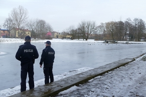 dwaj umundurowani policjanci stoją nad zamarzniętym stawem.