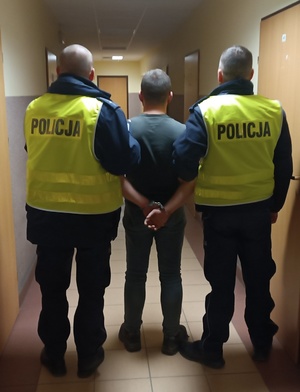 dwaj umundurowani policjanci prowadzą zatrzymanego mężczyznę.