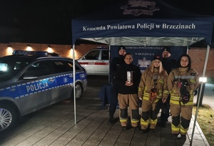 umundurowani policjanci i strażacy stoją z puszką WOŚP w policyjnym namiocie.