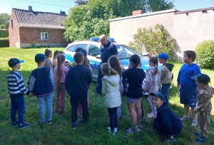 umundurowany policjant pokazuje przedszkolakom oznakowany radiowóz.