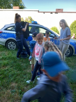 umundurowany policjant pokazuje przedszkolakom oznakowany radiowóz.