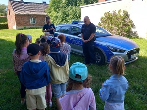 umundurowany policjant pokazuje przedszkolakom oznakowany radiowóz.