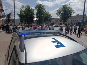 policyjny oznakowany radiowóz, a w tle uczestnicy przemarszu.