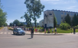 policyjny radiowóz wraz z dzielnicowym zabezpieczają uczestników przemarszu.