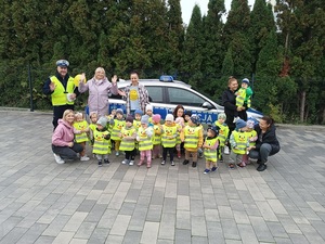 umundurowany policjant wraz z dziećmi pozuje do zdjęcia na tle oznakowanego radiowozu.