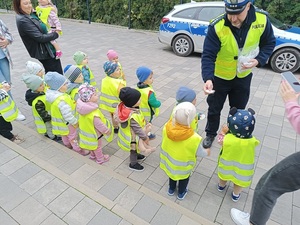 umundurowany policjant rozdaje dzieciom elementy odblaskowe.