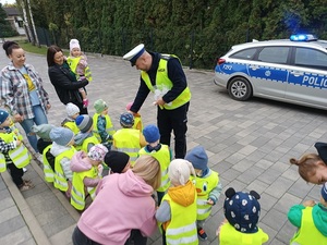 umundurowany policjant rozdaje dzieciom elementy odblaskowe.