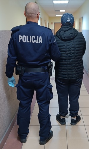 umundurowany policjant prowadzi zatrzymanego mężczyznę.