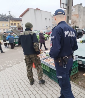 umundurowany policjant i przedstawiciel straży rybackiej kontrolują stoisko z rybami.