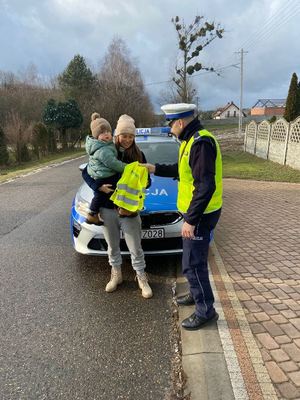 umundurowany policjant wręcza kamizelki odblaskowe.