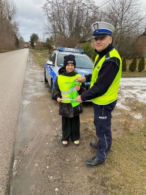 umundurowany policjant wręcza kamizelki odblaskowe.