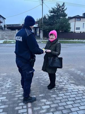 umundurowany policjant wręcza elementy odblaskowe napotkanemu seniorowi.