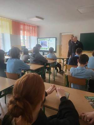 uczniowie ósmych klas słuchają prelekcji prowadzonej przez dyrektora i umundurowanego policjanta.