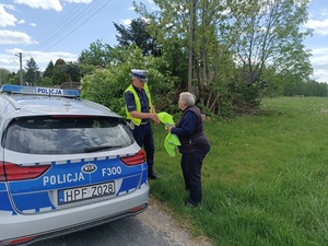 umundurowany policjant ruchu drogowego wręcza kamizelkę odblaskową niechronionemu uczestnikowi ruchu drogowego.
