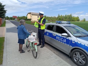 umundurowany policjant ruchu drogowego wręcza kamizelkę odblaskową niechronionemu uczestnikowi ruchu drogowego.
