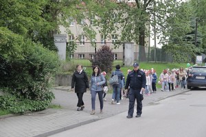 umundurowany policjant prowadzi grupkę dzieci.