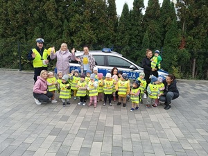 dzieci stoją wraz umundurowanym policjantem przy oznakowanym radiowozie.