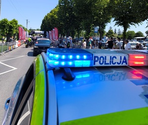 góra policyjnego oznakowanego radiowozu i biorący udział w wyścigu w tle.
