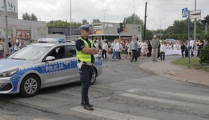 umundurowany policjant stojąc przy oznakowanym radiowozie zabezpiecza przejście procesji.