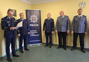 Komendant w galowym mundurze wręcza umundurowanym policjantom akty mianowania na wyższe stopnie policyjne.