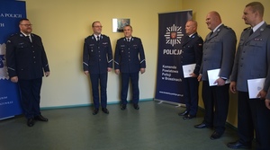 Komendant w galowym mundurze wręcza umundurowanym policjantom akty mianowania na wyższe stopnie policyjne.
