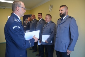 Komendant w galowym mundurze wręcza umundurowanym policjantom akty mianowania na wyższe stopnie policyjne.