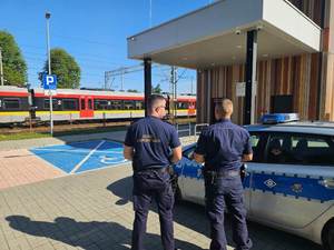 umundurowany policjant i strażnik ochrony kolei stoją na peronie stacji kolejowej.