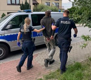 umundurowani policjanci prowadzą zatrzymanego mężczyznę.