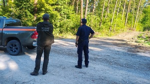 umundurowany policjant wraz z umundurowanym strażnikiem leśnym stoją obok samochodu leśników kontrolując dukty leśne.