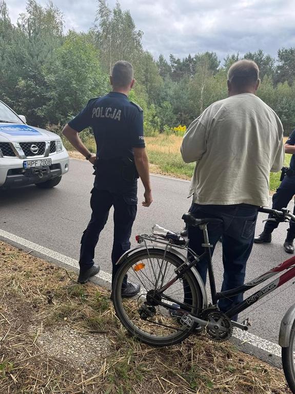 umundurowany policjant sto z poszukiwanym mężczyzną trzymającym przed sobą rower.
