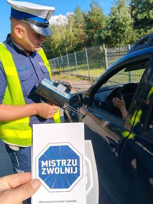 umundurowany policjanci podczas kontroli drogowej wręczają materiały promocyjne kampanii.