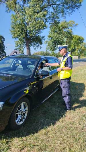 umundurowany policjanci podczas kontroli drogowej wręczają materiały promocyjne kampanii.