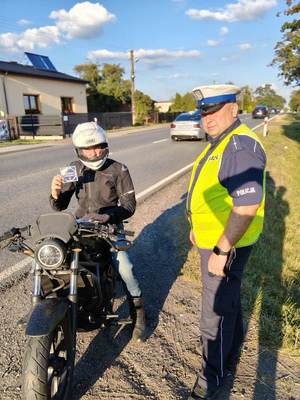 umundurowany policjanci podczas kontroli drogowej wręczają materiały promocyjne kampanii.